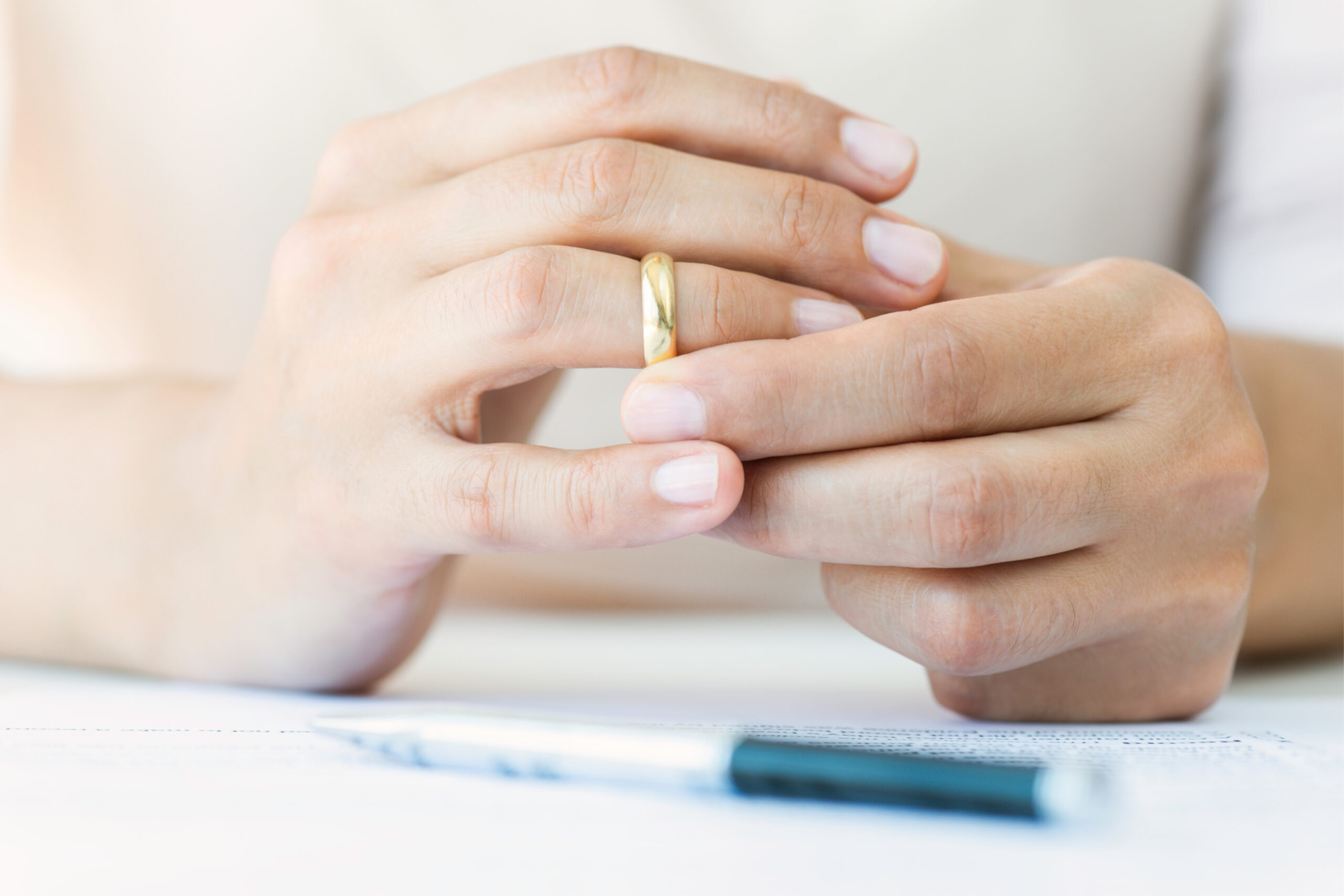 woman taking off her wedding ring after signing her divorce papers with her attorney